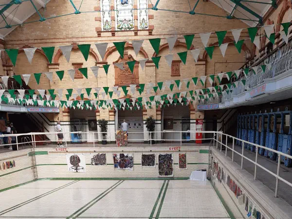 An empty swimming pool with green lane markers and colorful decorations, under a glass roof. — Victoria Baths, Manchester